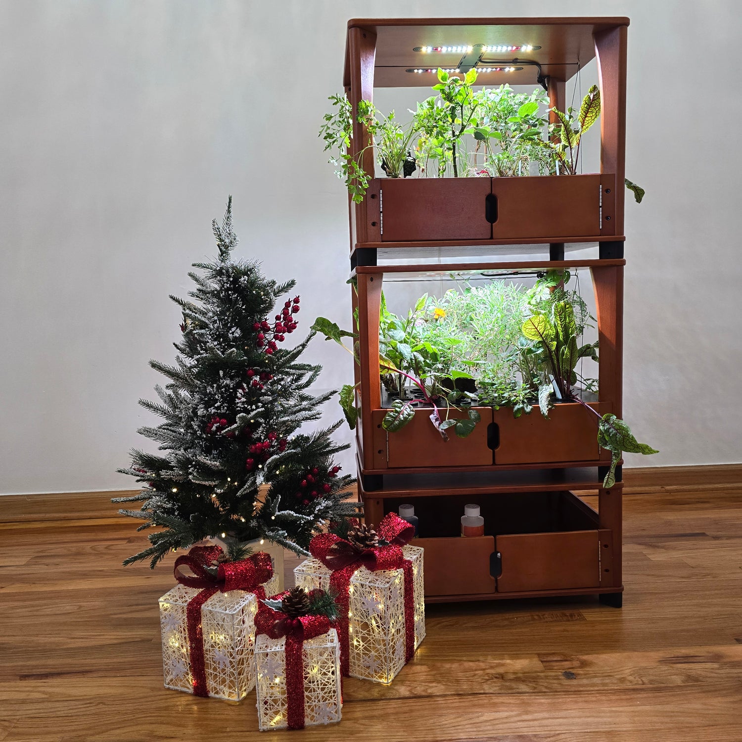 Decorative Christmas tree with lights and presents in front of a wooden cabinet with glass doors.