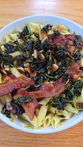 Pasta dish with bacon and greens in a white bowl on a wooden table