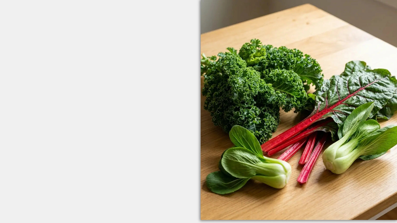 Assorted green vegetables including kale, bok choy, and radishes on a wooden cutting board.