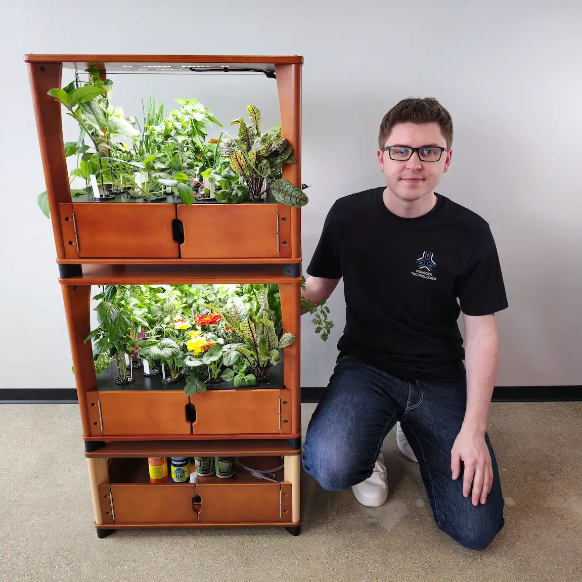 Person kneeling next to a wooden indoor garden system with plants.
